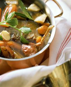 Beef broth with soup vegetables and herbs in copper pan