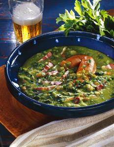 Pea soup with bacon and sausages in blue soup bowl