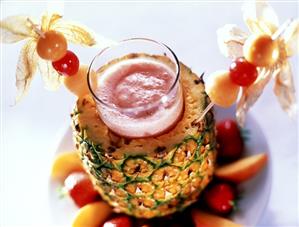 Fruity strawberry cocktail in glass in hollowed-out pineapple