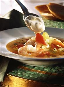 Vegetable soup with shrimps, sour cream on spoon above it