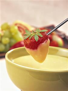 White chocolate fondue with strawberry on fondue fork