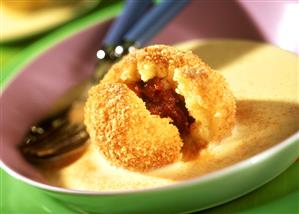 Plum dumplings with custard sauce on plate with cutlery