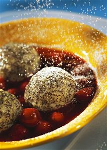 Icing sugar falling on poppyseed dumplings with cherry sauce