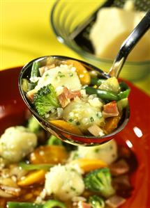 Vegetable soup with chive dumplings on ladle above plate