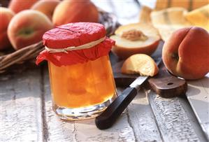 Peach preserve in jam jar in front of fresh peaches