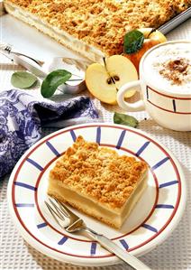 Apple cake with crumble on plate & baking sheet; cappuccino