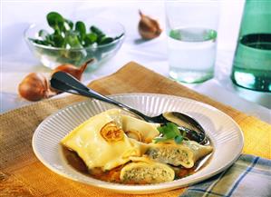 Pasta envelopes (Maultaschen) in soup plate; corn salad; onions