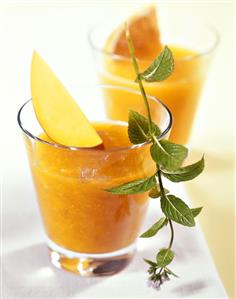 Mango smoothie in glasses with sprig of mint