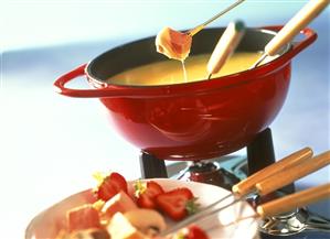 Cheese fondue with ham and strawberries in fondue pot