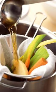 Making vegetable stock: straining broth over vegetables