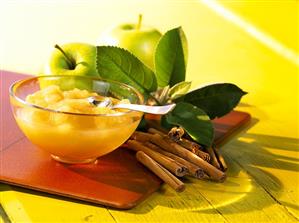 Apple compote in bowl; cinnamon sticks; fresh apples