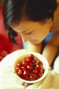 Young woman bending over bowl of red cherries