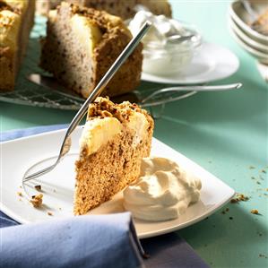 Piece of warm apple cake with cream in front of cake, piece cut