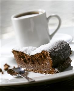 A piece of chocolate cake, a cup of coffee behind