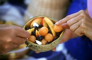 Hands reaching for pieces of fruit salad in halved melon