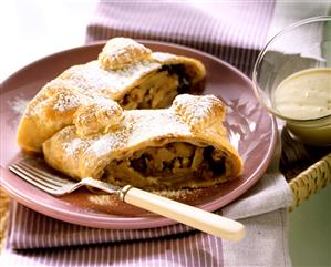 Apple strudel on a plate, custard in a bowl beside it