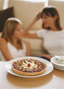 Fruit cake on table, woman and girl on sofa behind