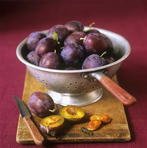 Fresh plums in and beside a colander on a chopping board