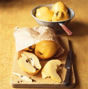 Quinces (whole and sliced) in paper bag on chopping board