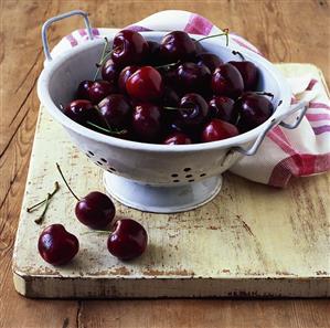 Red cherries in a colander on an old wooden chopping board