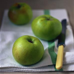 Three Granny Smith apples on tea towel with knife