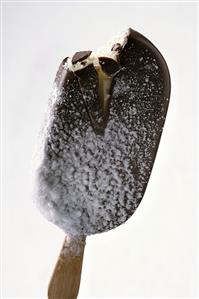 Chocolate-coated vanilla ice cream on stick, frosted (a bite taken)