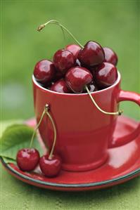 Cherries in red cup and saucer on table out of doors