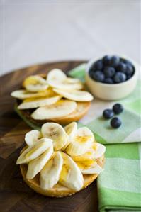 Banana slices and honey on bread roll, dish of blueberries