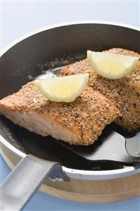 Fried salmon fillet with lemon wedges in frying pan