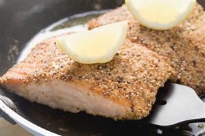 Fried salmon fillet with lemon wedges in frying pan