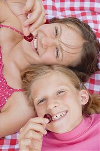 Two girls with cherries on a picnic cloth