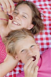 Two girls with cherries on a picnic cloth