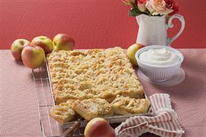 Apple crumble cake on baking tray, cream, fresh apples