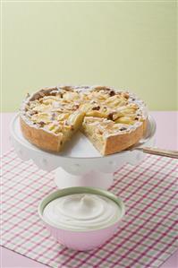 Apple tart with flaked almonds, a piece cut, whipped cream