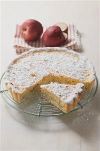 Apple tart with icing sugar, a piece cut, on cake rack