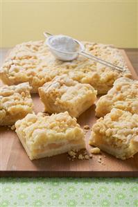 Apple crumble tart, pieces cut, icing sugar in sieve