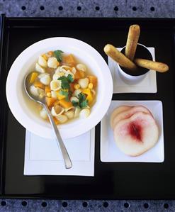 Noodle soup with vegetables, bread sticks and peach slices