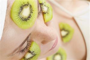 Young woman with slices of kiwi fruit on her face and neck