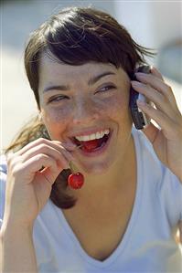 Young woman with a pair of cherries and a mobile phone