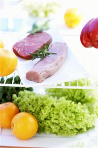 Pork fillet, beef steak, lettuce and fruit in refrigerator