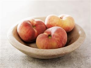 Three flat peaches in a bowl