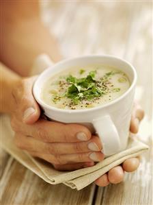 Hands holding a cup of creamed vegetable soup