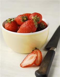 Strawberries in a bowl with halved strawberry and knife