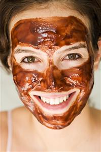 Woman with chocolate face mask eating a bar of chocolate