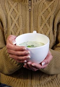 Two hands holding a cup of broccoli cream soup