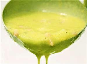 Pea soup with bacon dripping from a ladle