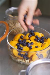 Hand scattering blueberries into a bowl for peach gratin