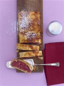 A partly-sliced cherry strudel on a wooden board