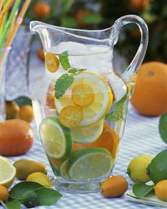 Jug of water with citrus fruit, lemon balm and ice cubes