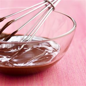 Melted chocolate in a glass bowl with a whisk